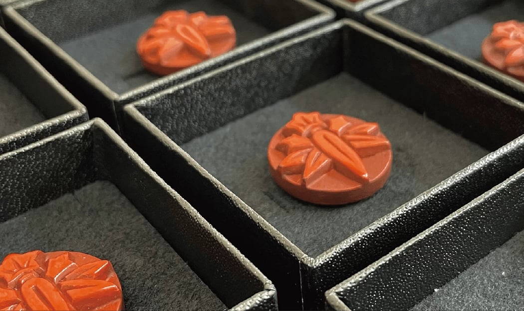 ▲職員バッジは、カツラやイチョウの木でつくられており、市のシンボルである「ササリンドウ」があしらわれている。